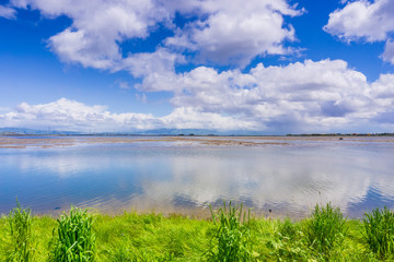 Cloudscape reflected in the ponds; Dumbarton bridge and office buildings in the background; Bedwell Bayfront Park, Menlo Park, San Francisco bay area, California