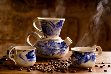 Alternative coffee brewing method, using pour over dripper and paper filter.. Two cups of coffee and a coffee pot on a wooden table. Coffee beans on a table. 