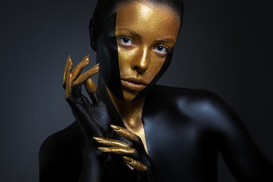 Beautiful girl with gold and black paint on her face and body. Female portrait with creative makeup.