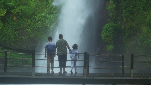 Young father and his children enjoying holiday by looking at Sawer Waterfall in Sukabumi, West Java, Indonesia. Shot in 4k resolution