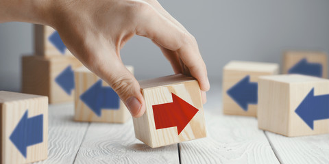 Hand putting a wooden cube with red arrow showing the opposite to blue arrows direction on neutral background - obrazy, fototapety, plakaty