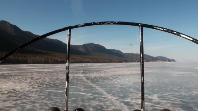 Airboat air glider moves on ice on background of winter landscape with mountain coast and clear blue sky of Lake Baikal in Siberia.