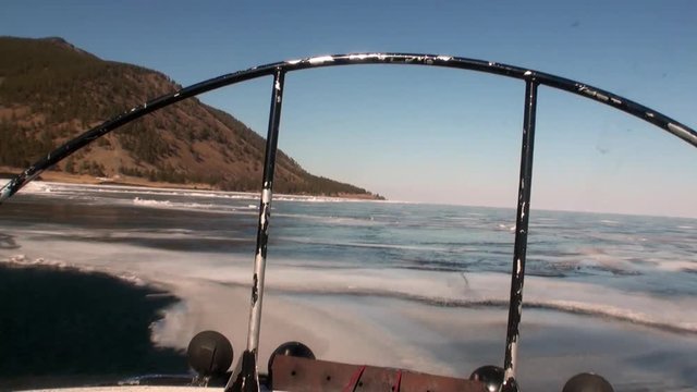 View from of moving airboat air glider on smooth ice on background of winter landscape with mountain coast and clear blue sky of Lake Baikal in Siberia.
