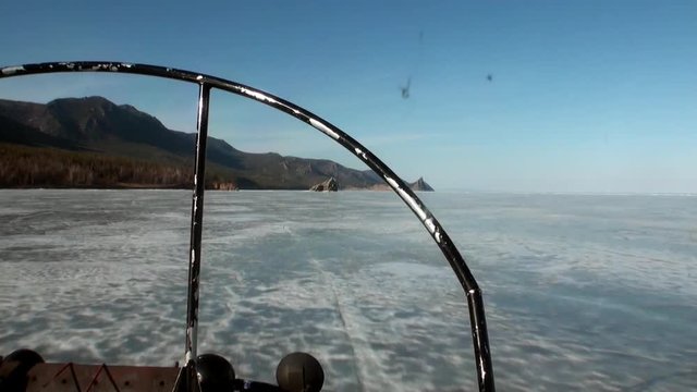 Moving airboat air glider on ice on background of winter landscape with mountain coast and clear blue sky of Lake Baikal in Siberia.