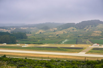 Aerial view of agricultural fields, local airport runway and hills covered in fog, Moss Beach,...
