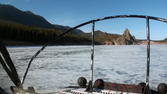 Airboat air glider moves to mountain coast on ice on background of winter landscape and clear blue sky of Lake Baikal in Siberia.