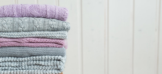 Stack of cozy knitted clothes on a wooden ladder. Web banner Scandinavian style. White wooden wall
