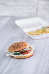 tasty delicious hamburger in box with French fries and vegetable, grey background, wood pattern, light picture, close up of meal, unhealthy fast food option for eating