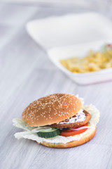 tasty delicious hamburger in box with French fries and vegetable, grey background, wood pattern, light picture, close up of meal, unhealthy fast food option for eating