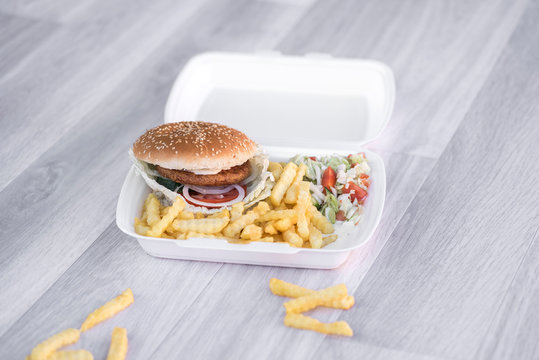 tasty delicious hamburger in box with French fries and vegetable, grey background, wood pattern, light picture, close up of meal, unhealthy fast food option for eating
