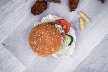 tasty delicious hamburger in box with French fries and vegetable, grey background, wood pattern, light picture, close up of meal, unhealthy fast food option for eating