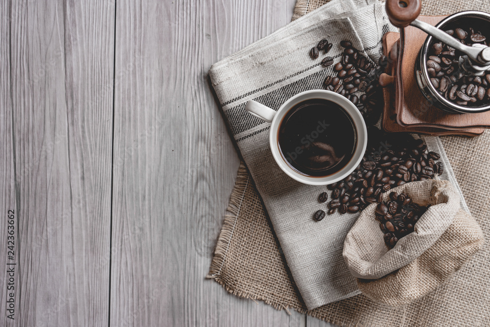 Wall mural black coffee in a coffee cup with coffee beans and coffee grinder on wooden table. top view