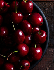 Top view of cherries in a black bowl over a wood table