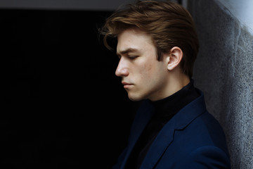 Obraz premium Portrait of a handsome, attractive, young man in a blue suit, coat, in the city. pensive and sad, waiting.