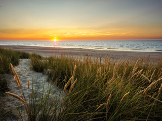 Sun setting in the sea in front off colorful marram grass covered dunes in northern France
