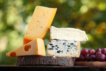 Camembert, brie, hard cheese and blue cheese on a wooden board. Slices of various cheeses and grapes on a blurred background. Dorblu and soft cheese on wooden boards. Cheese and grapes on bokeh