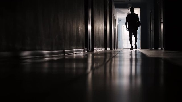 Silhouette of sportsman walking along hallway and dribbling basketball 