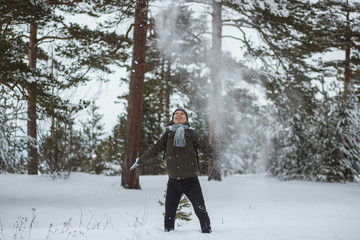 Portrait cheerful man in winter pine forest. He blowing snow up from gloves in winter day