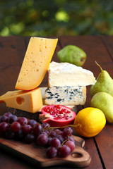 Camembert, brie, hard cheese and grapes on a wooden stand. Pieces of different cheeses, pear and lemon on blurred background. Dorblu, soft cheese and pomegranate on boards. Cheese and fruit
