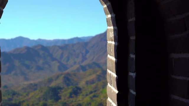 Steadicam shot of the Chinese Great wall that rises up the side of the mountain in a begining of fall. Camera moves through the passage in the watchtower and shows the view from the window on the wall