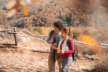 Cute smiling Caucasian couple hiking. Woman holding map, on backs backpacks.