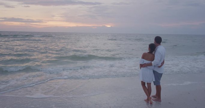 Honeymoon couple relaxing on beach looking at sunset embracing in love on travel vacation. Serene calm scene shot in SLOW MOTION on RED cinema Camera.