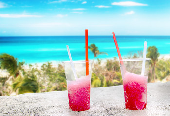 Two strawberry red drift-ice with straw on the beach. In the background is blue sky, palms, sea nd sandy beach. This is situated in tropical resort in Thailand © Jana