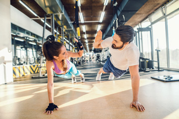 Sporty couple doing push-ups and giving high five. Gym interior.