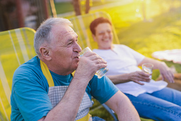 Picture of older happy couple resting in chair in their backyard. Talking and smiling.