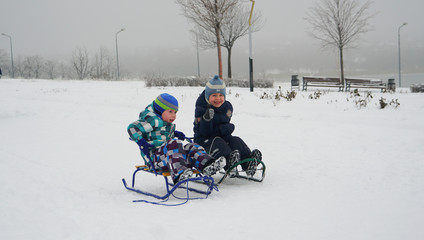 Two little children sledding on the snow-covered road in winter