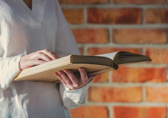 Woman in white shirt holding old book on brick wall background