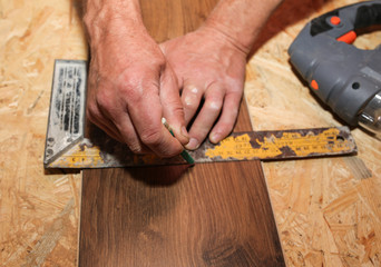 Worker is holding in hands a try square for measuring. Power jigsaw for laminate flooring. Maintenance repair works renovation in the flat with scroll saw. Restoration of wooden parquet floor planks.