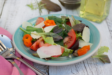 Home made fresh salad with parmezan cheese, greens and tomato. White rustic wooden table. Top view.