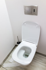 Modern toilet in public toilet with toilet paper on ground, clean white minimalist background interior with open bowl closeup, flush button