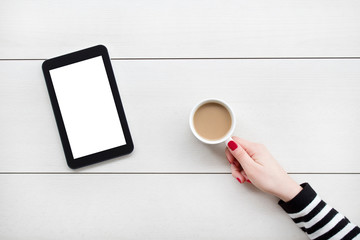 Woman hand holding digital tablet and coffee on white desk.