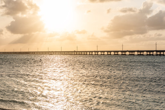 Seven Mile Bridge landscape of Florida Keys reflection of sun on water atlantic ocean and Overseas Highway road with horizon clouds sunset rays