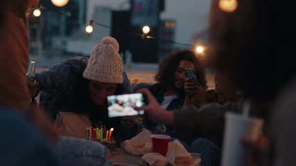 happy group of friends celebrating birthday party on rooftop at sunset beautiful young woman blowing candles enjoying celebration making toast to friendship 
