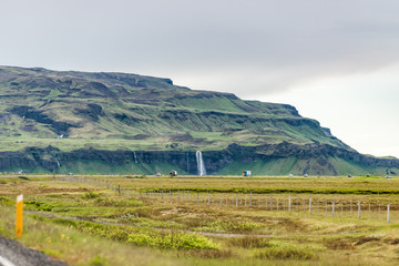 Iceland Mountains landscape view of cars on road trip by green mountain and southern ring road or golden circle and Seljalandsfoss waterfall far