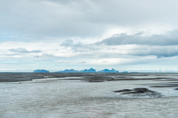 Landscape view of Heimaey island in southern region in Iceland in distance from Seljalandsfoss with river water and cloudy stormy overcast sky black sand