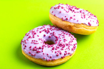 Two delicious lilac donuts with sprinkle on bright green background