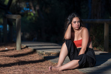 Mujer joven morena sentada descalza en el bosque mirando a cámara