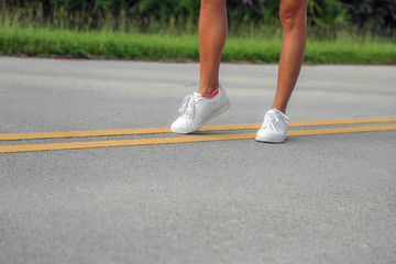 Fototapeta premium Tanned sporty female legs in white sneakers on the asphalt road on the yellow strip