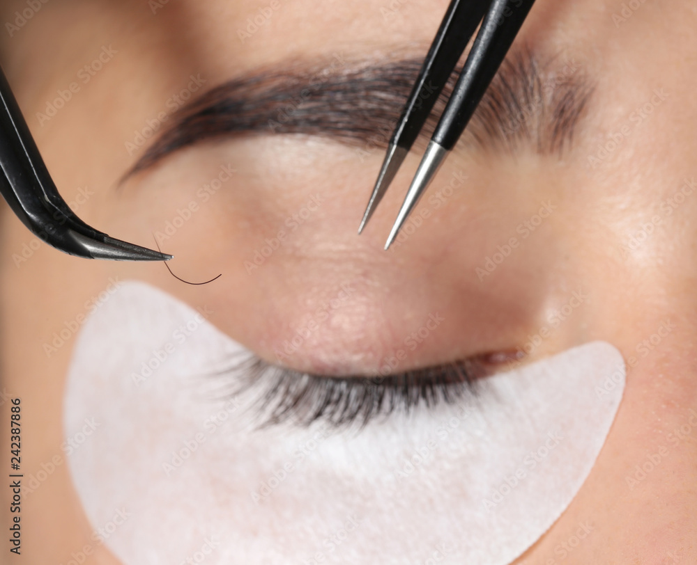 Sticker Young woman undergoing eyelashes extensions procedure, closeup