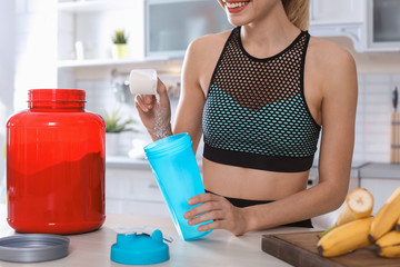 Young woman preparing protein shake at table in kitchen, closeup