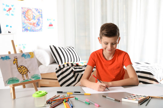 Little child drawing picture at table with painting tools indoors
