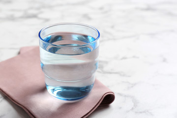 Glass with fresh water and napkin on marble table. Space for text