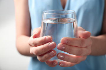 Woman holding glass with fresh water against light background, closeup