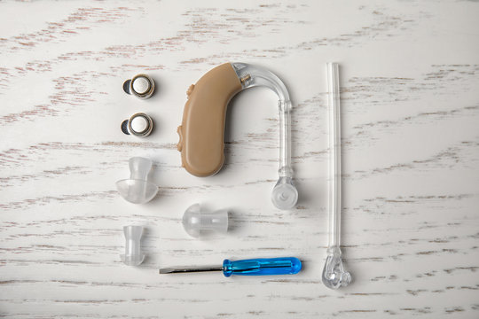 Flat lay composition with hearing aid and accessories on white wooden background