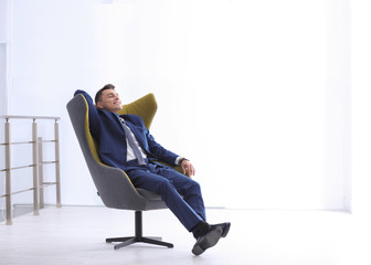 Young businessman sitting in comfortable armchair indoors. Space for text
