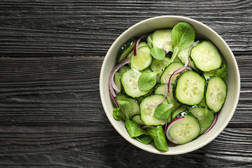 Delicious cucumber salad with onion and spinach in bowl on wooden background, top view. Space for...